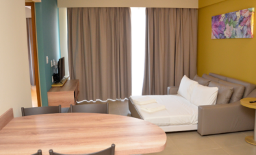 Sala com sofá-cama aberto, TV, varanda e mesa de cozinha americana em ambiente integrado e funcional